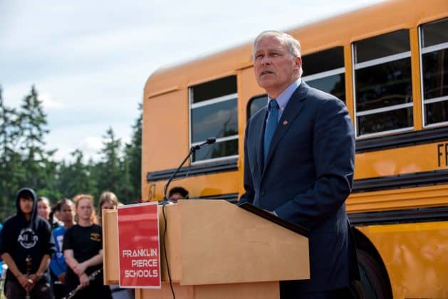 Speaker Gov. Inslee. stands in front of a new all-electric Blue Bird school bus.