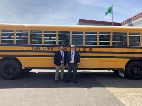 Two district officials stand in front of a new all-electric Blue Bird school bus.