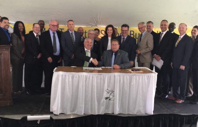Signing of the agreement by Michigan Department of Environment, Great Lakes, and Energy’s Jack Shinderle, left at table, and David Meeuwsen, director of transportation for Zeeland Public Schools, right. Directly behind Meeuwsen is Michigan Gov. Gretchen Whitmer and Quebec Assistant Deputy Minister of International Affairs and La Francophonie Eric Marquis. They’re surrounded by stakeholders from government, school districts, and utilities who art partners in the the Michigan Association for Pupil Transportation Electric School Bus Pilot Project.