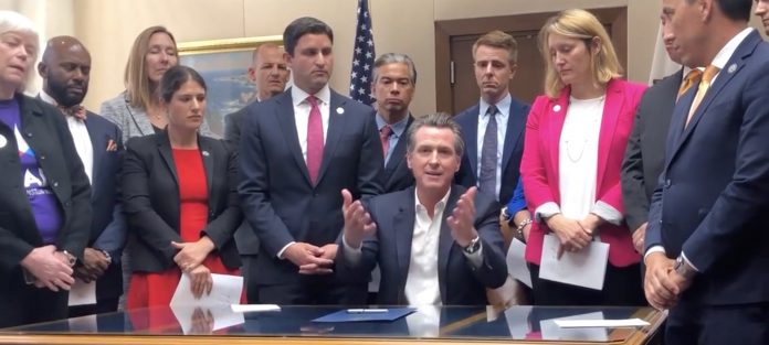 Gov. Gavin Newsom (center) signed many bills into law on Oct. 13, including the controversial school start time bill. (Screen capture of video by the Sacramento Bee.)