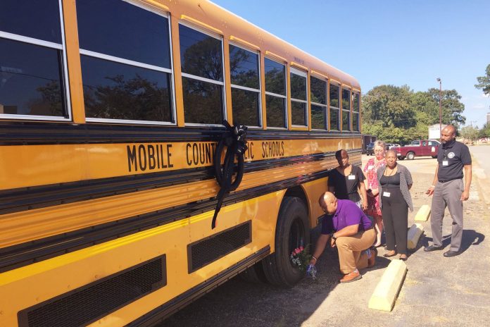 Pat Mitchell, Mobile County Public Schools director of transportation, places flowers on a school bus wheel in memory of driver Kimberleigh Welch, who died in a crash on Oct. 10, 2019. (Facebook/Mobile County Public Schools.)