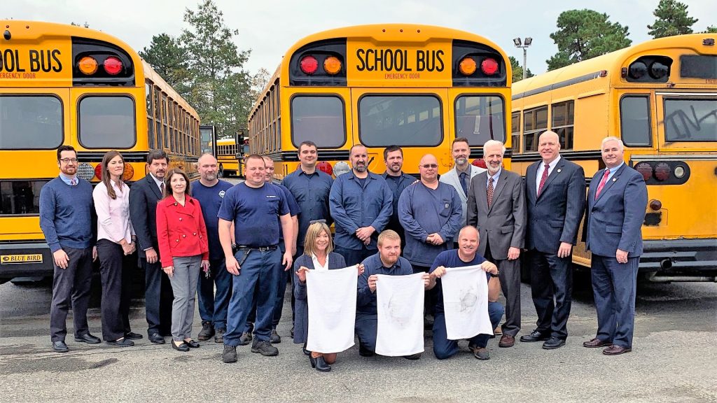 EPA reps stand with district administrators and transportation personnel after the EPA conducted its "white hanky" test, exhibiting the difference in emissions from an old diesel bus (far right) with newer-model gas (far left) and propane vehicles.