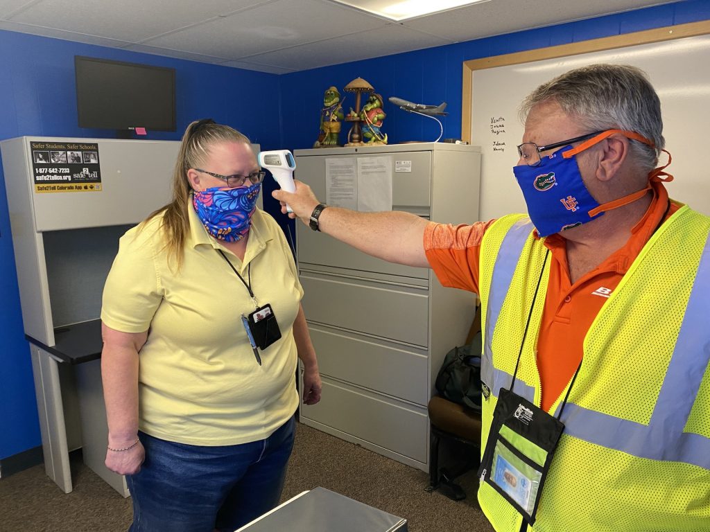 A Denver Public Schools transportation employee checks his coworker's temperature with a contactless thermometer.