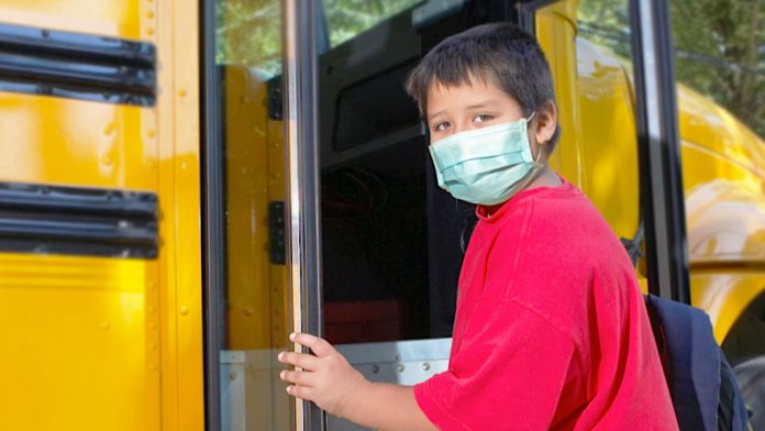 boy with COVID-19 mask boards school bus