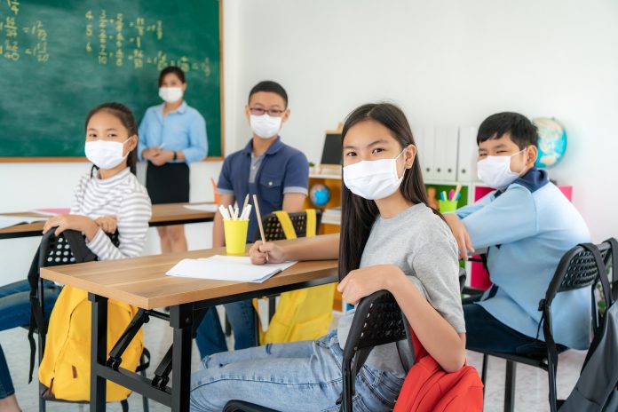 Group of Asian elementary school students and teacher wearing hygienic mask to prevent the outbreak of Covid 19 in classroom while back to school reopen their school, New normal for education concept.