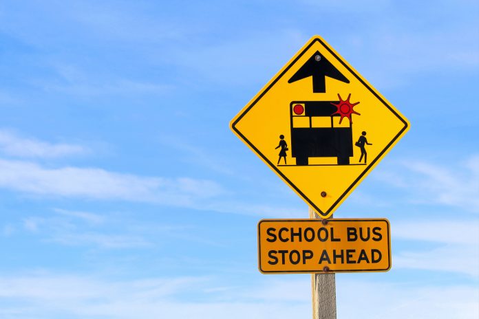 Closeup of a School Bus Stop Ahead Sign Against a Blue Sky