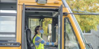 Female bus driver wearing a protective face mask and shield while driving a school bus during COVID-19 to avoid the transfer of germs.