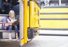 Schoolgirl sitting in school bus and reading the book. Back to school or education concept