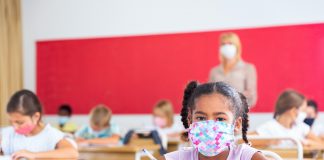 Portrait of focused schoolgirl wearing protective face mask working at lesson in classroom, writing exercise
