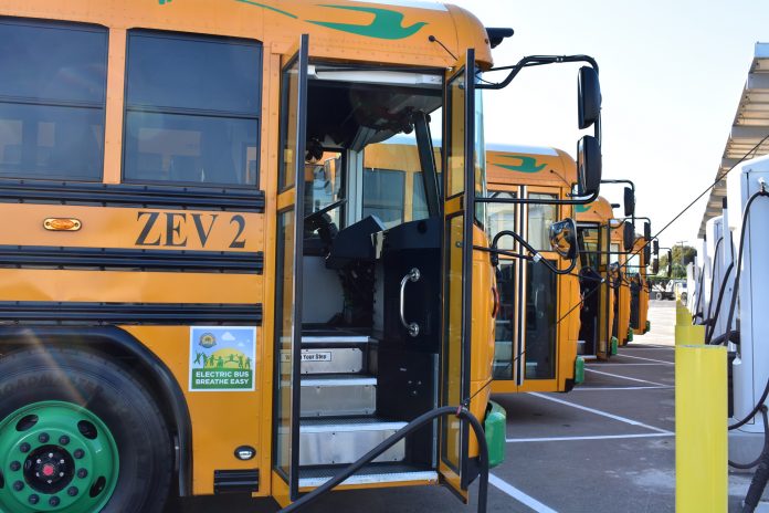 A row of electric school buses charge at Stockton Unified School District in California.