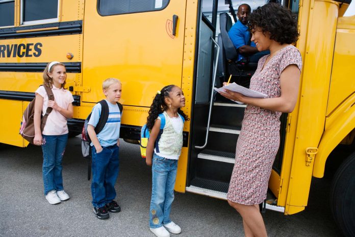 Female teacher taking a note of students before boarding school bus.