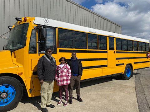 Staff from Fairfield City Schools in Alabama stand with the district's new electric school bus. From left: School bus driver Edell Brewer; Aretha Brewer, administrative assistant for transportation; and Richard Fuah, assistant transportation director. (Photo courtesy of Malinda Sandu.)