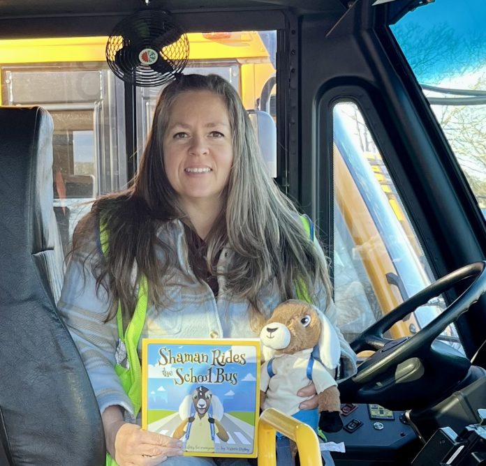 School bus driver Valerie Higley poses with her published book “Shaman Rides the School Bus,” to teach safety to children and their parents. Shaman the Goat plushie is also available for pre-order.